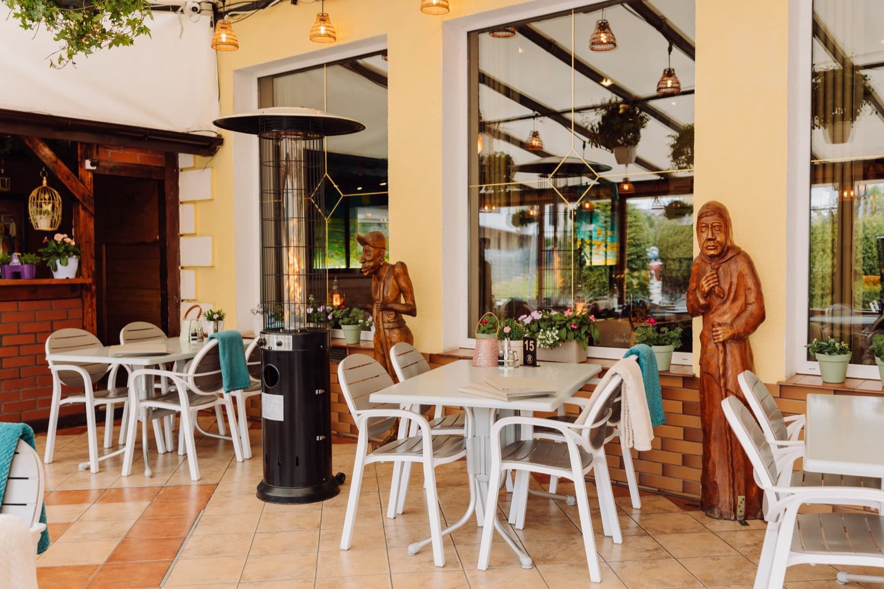Przeszklony, zadaszony taras restauracji z białymi krzesłami i roślinami